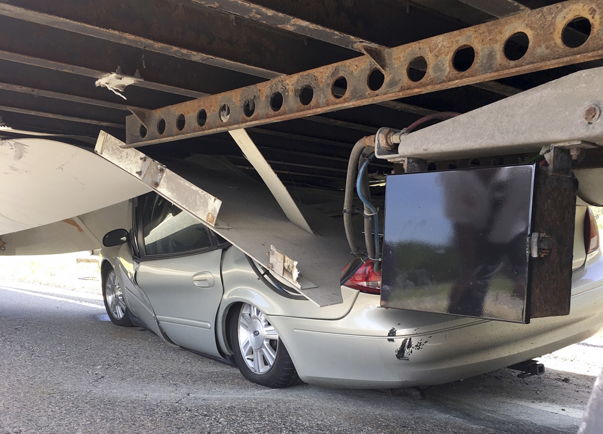 In this photo released Tuesday, July 16, 2019 by the Uxbridge Fire Department on its Facebook page, a car sits wedged under a tractor-trailer on Route 146 in Uxbridge, Mass. The motorist, whose name wasn't made public, climbed out of the driver's side door of the crushed car and wasn't seriously hurt. (Uxbridge Fire Department via AP)