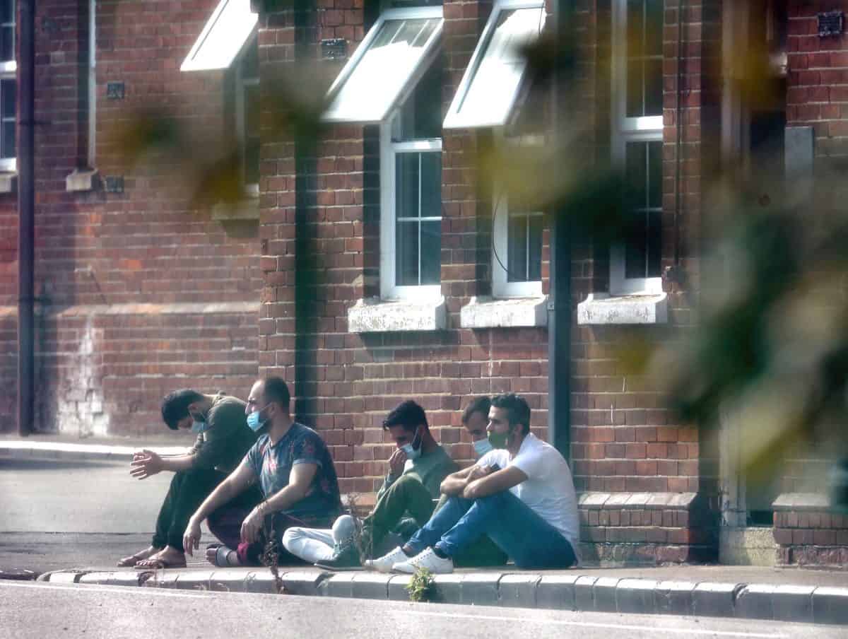 A group of men, thought to be migrants, sit outside in the sunshine after arriving yesterday night at Napier Barracks in Folkestone, Kent. Migrants will be housed in the military barracks from this week while their asylum claims are processed.